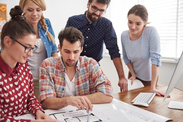 Colegas de trabalho no escritório com planos de arquitetura e um computador