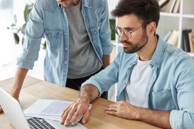 Colegas discutem novas ideias para aumentar lucros, com foco em laptop, cercado de documentos