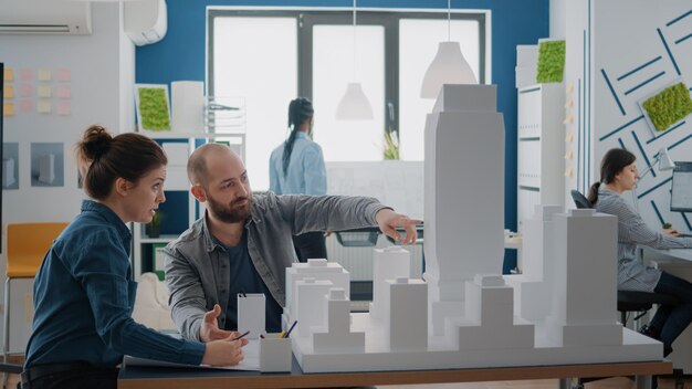 Colegas fazendo trabalho em equipe na concepção do plano de plantas depois de analisar o modelo de construção. Equipe de pessoas usando maquete para criar construção arquitetônica para projeto de desenvolvimento urbano.