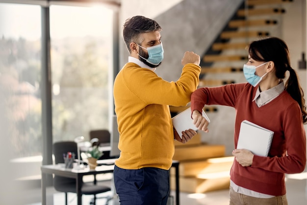 Colegas felizes usando máscaras faciais e cotoveladas no escritório