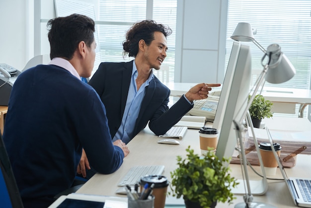 Colegas masculinos asiáticos olhando para a tela do computador juntos no escritório