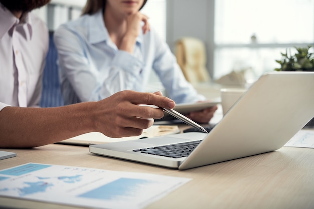 Colegas masculinos e femininos irreconhecíveis, olhando para a tela do laptop no escritório