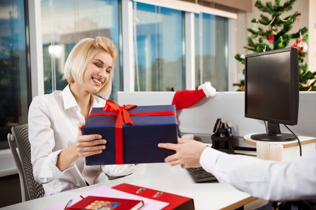 Colegas que comemoram a festa de Natal no escritório que sorri dando presentes.