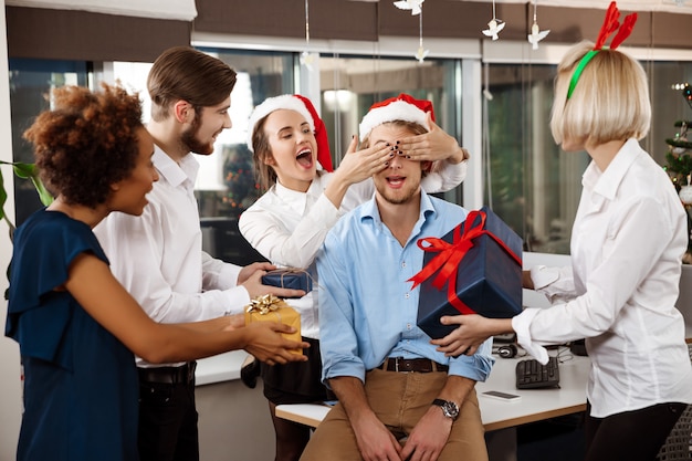 Colegas que comemoram a festa de Natal no escritório que sorri dando presentes.