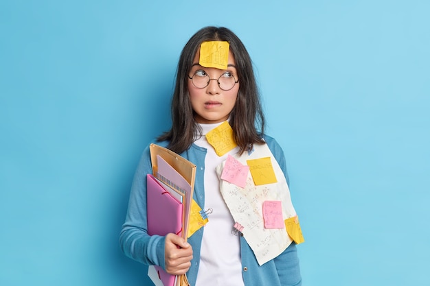 Foto grátis colegial pensativa e intrigada se prepara para os exames na escola morde os lábios e, concentrada ao lado, tenta aprender informações antes que a prova de matemática use óculos redondos para correção da visão.