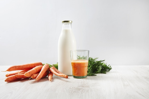 Colheita de cenoura de fazenda orgânica perto da garrafa com leite e meio copo cheio de suco natural fresco no café da manhã.