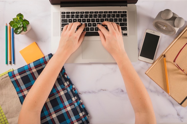 Foto grátis colheita de mãos digitando no laptop perto de amostras de pano