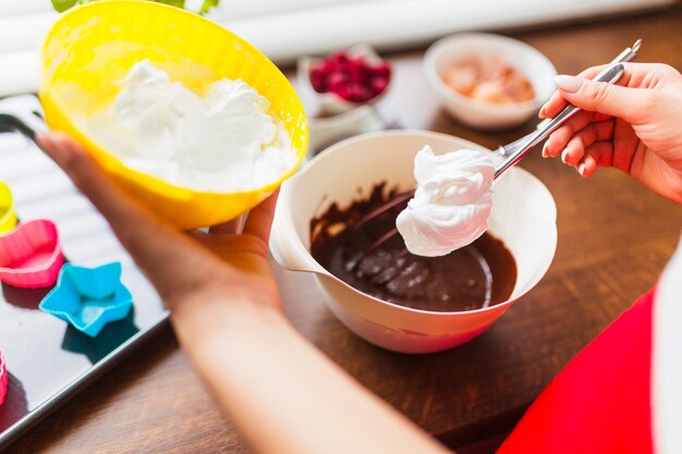 Colheita mulher adicionando creme chicoteado em massa