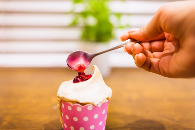 Colher mão derramando geléia no cupcake