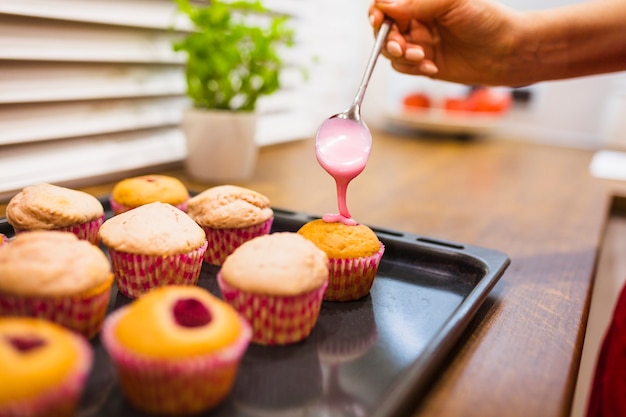 Colher mão derramando molho em muffins