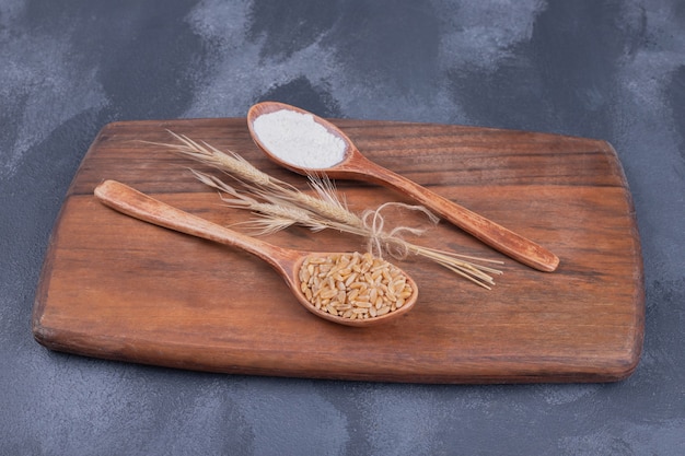 Colheres com espiga de trigo e farinha na placa de madeira.