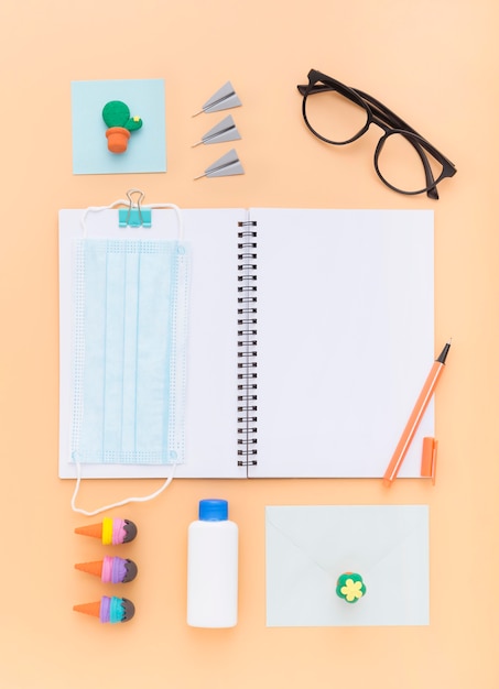 Colocação plana de materiais escolares com caderno e máscara facial