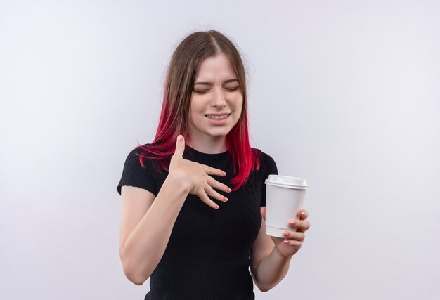 Com os olhos fechados, bela jovem vestindo uma camiseta preta segurando uma xícara de café na parede branca isolada