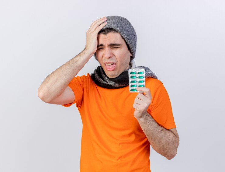 Foto grátis com os olhos fechados, jovem doente com chapéu de inverno e lenço segurando comprimidos
