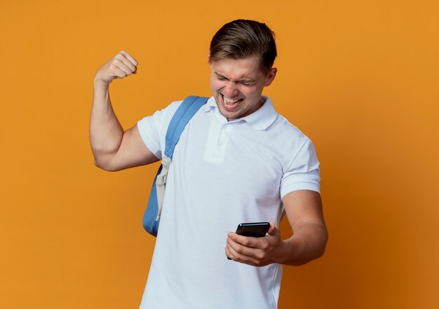 Com os olhos fechados, jovem e alegre estudante do sexo masculino usando uma bolsa nas costas segurando o telefone