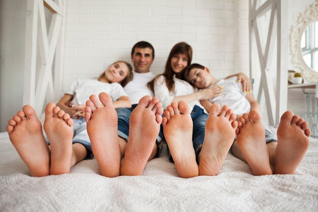 Com os pés descalços de família feliz sentados juntos na cama em casa