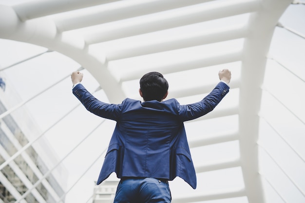 Foto grátis com sucesso, o jovem empresário mantém os braços erguidos e expressando positividade enquanto fica ao ar livre