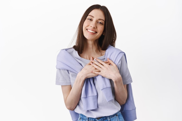 Com todo o meu coração tocada e agradecida linda garota sorrindo de mãos dadas no coração expressa gratidão em pé sobre fundo branco