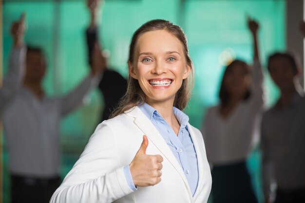 Com um largo sorriso Mulher de negócios que mostra o polegar para cima