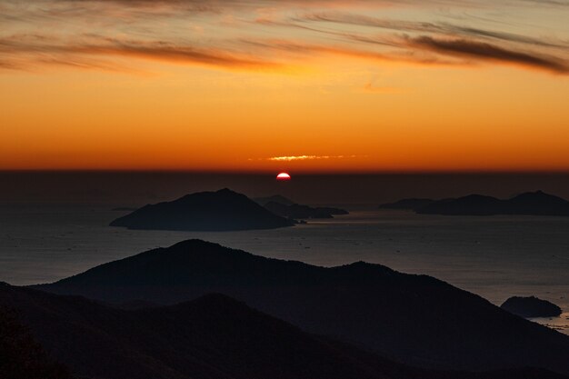 Com vista para uma silhueta de montanhas no mar durante o pôr do sol