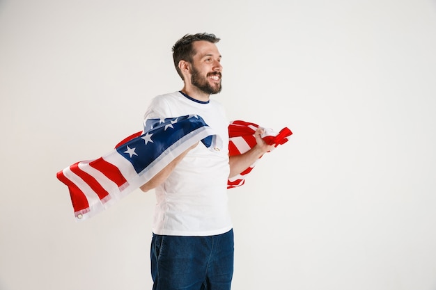 Comemorando o dia da independência. estrelas e listras. jovem com bandeira dos estados unidos da américa, isolada na parede branca do estúdio. parece muito feliz e orgulhoso como um patriota de seu país.