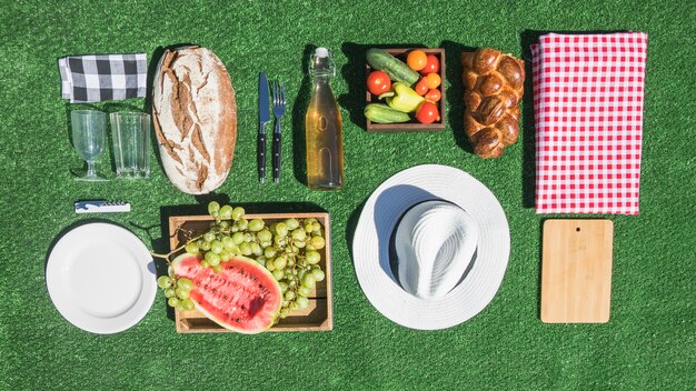 Comida de piquenique; pão; frutas; placa; tábua de cortar; toalha de mesa no relvado verde