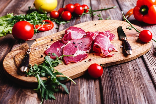 Comida fresca e saudável. Carne vermelha fatiada situa-se na mesa de madeira com rúcula