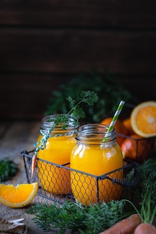 Comida saudável. cenouras e suco de cenoura com laranja em uma jarra de vidro em uma cesta de metal em um fundo escuro de madeira. copiar espaço
