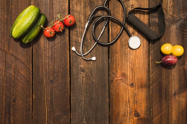 Comida saudável com estetoscópio e cinta de aptidão no cenário de madeira