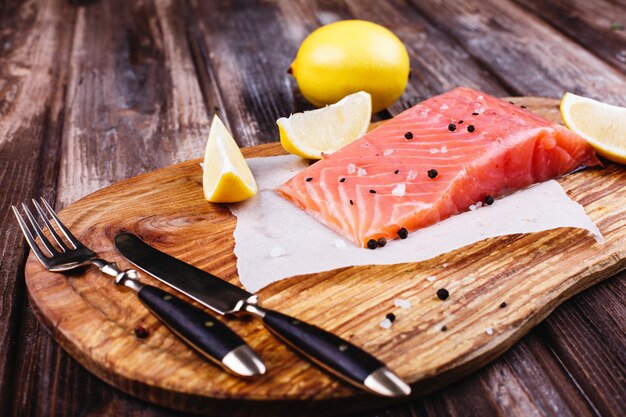 Comida saudável e fresca. Salmão cru servido com limões e facas na placa de madeira