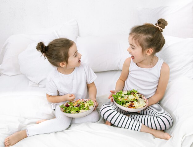 Comida saudável em casa. Felizes dois filhos bonitos comendo frutas e legumes no quarto na cama. Alimentação saudável para crianças e adolescentes.