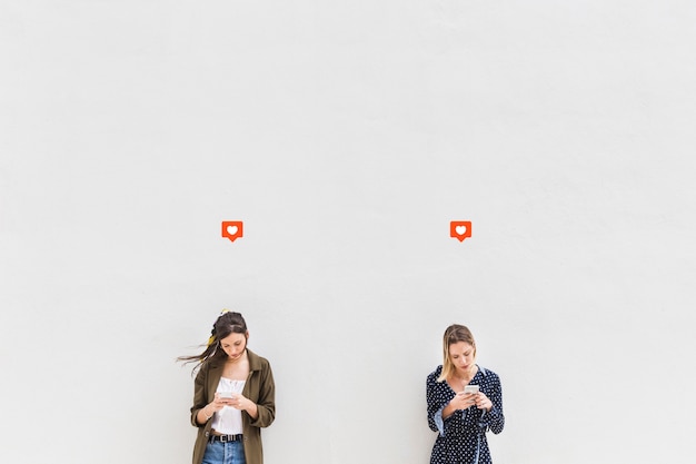 Foto grátis como ícone sobre as duas jovens mulheres usando telefones celulares contra o fundo branco