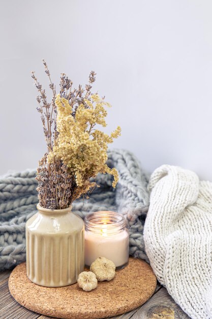 Composição aconchegante com um vaso de flores secas, uma vela e um elemento de malha