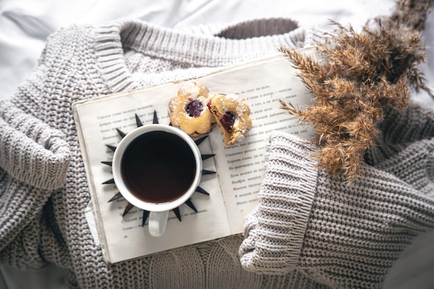 Composição caseira com uma xícara de café, biscoitos, um livro e um suéter tricotado