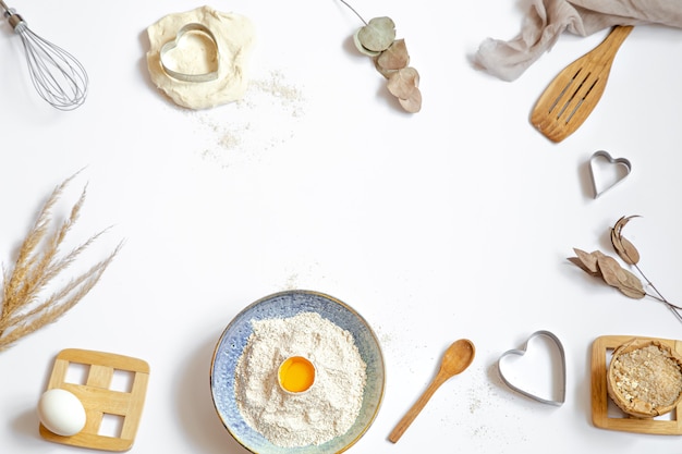 Composição com ingredientes de cozimento e acessórios de cozinha em uma mesa branca.