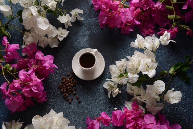 Composição com xícara de café branca, feijão e flores como pano de fundo