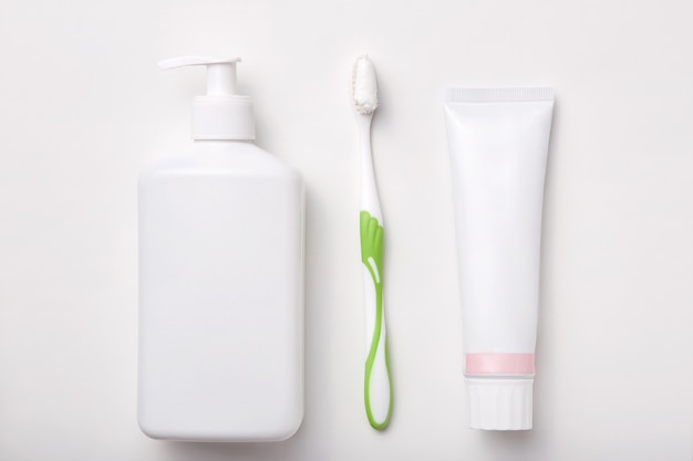 Composição da escova de dentes, creme dental e garrafa de sabão ou gel isolado no branco. Produtos cosméticos. Configuração plana