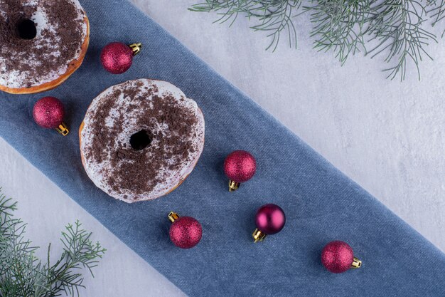 Composição de deliciosos donuts e decorações de natal em uma toalha de mesa dobrada em fundo branco.