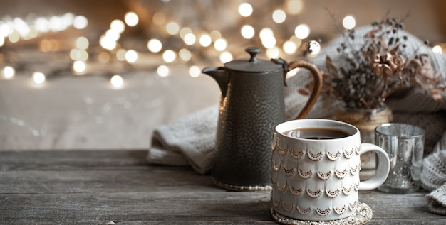 Composição de inverno com uma bela xícara de bebida quente e um bule em um fundo desfocado com bokeh.