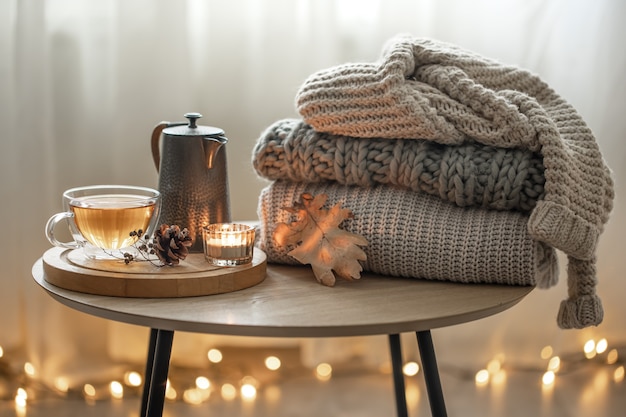 Composição de outono em casa com chá e camisolas de malha no interior da sala, em um fundo desfocado com uma guirlanda.