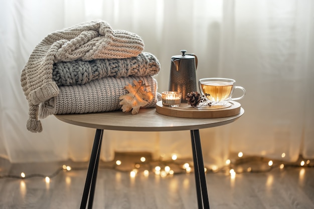 Composição de outono em casa com chá e camisolas de malha no interior da sala, em um fundo desfocado com uma guirlanda.