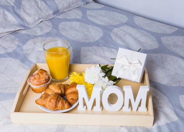 Foto grátis composição de padaria perto de vidro, flores e mãe palavra na bandeja na cama