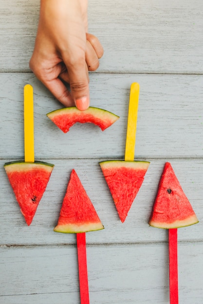 Foto grátis composição de verão com mão segurando uma peça de melancia mordida