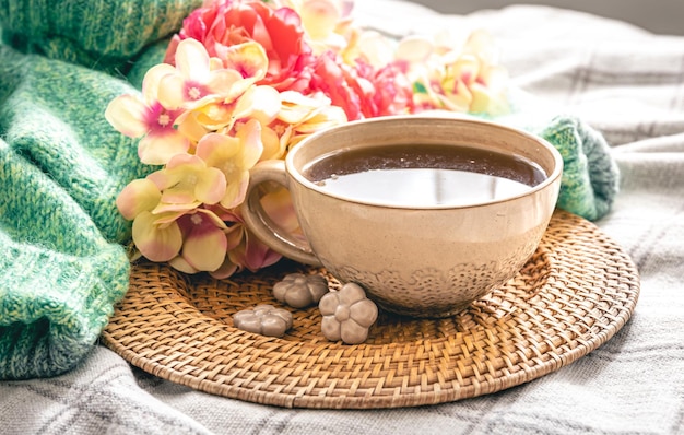 Composição doméstica com uma xícara de flores de chá e um elemento de malha na cama