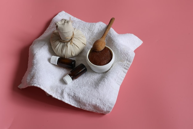 Composição minimalista de spa com saco de massagem de ervas, frascos de esfoliante natural e óleo no fundo rosa, copie o espaço.
