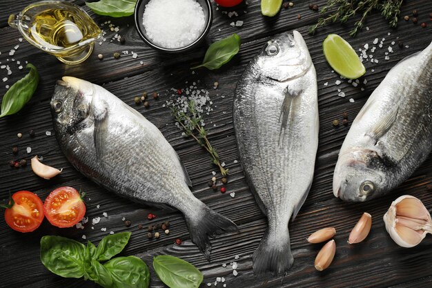 Composição plana leiga com peixe cru dorada na mesa de madeira preta