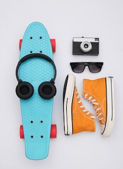 Composição plana leiga de acessórios de jovens hipster. placa cruzadora, tênis, fones de ouvido, câmera e óculos de sol em um fundo branco. vista do topo