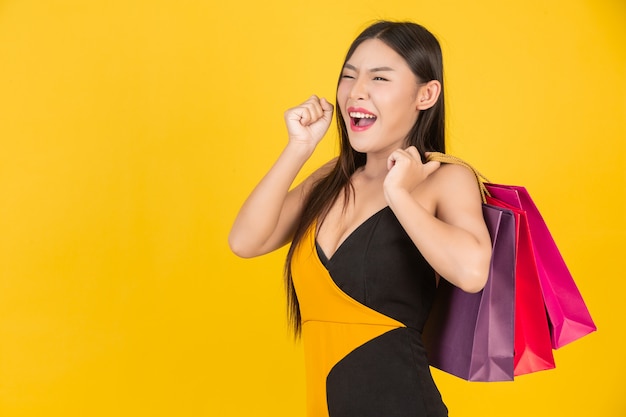 Compra linda mulher segurando um saco de papel colorido em um amarelo.