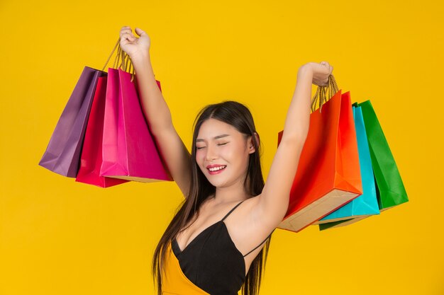 Compra linda mulher segurando um saco de papel colorido em um amarelo.