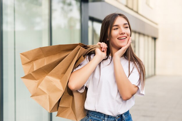 Comprador espantado abrindo a boca segurando sacolas de compras, vendo ofertas especiais em lojas e apontando na rua